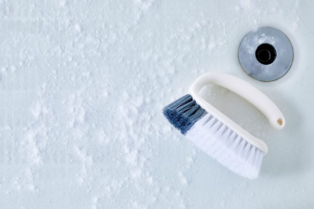 cleanser distributed on the bathtub surface, a scrub brush nearby