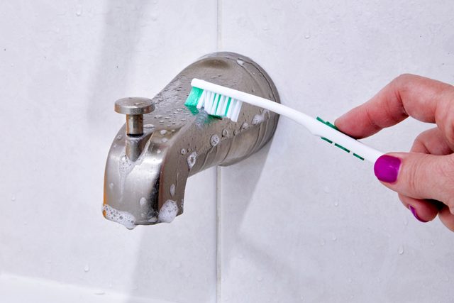 hand using a toothbrush to clean the tub spout