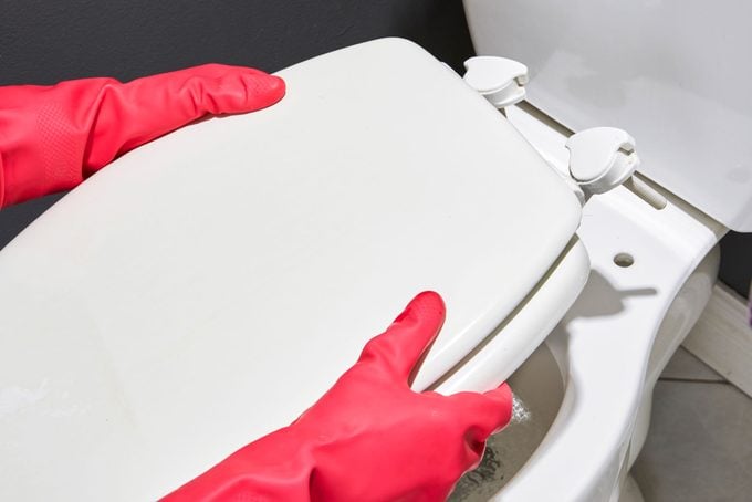 gloved hands removing the toilet seat and cover from the toilet