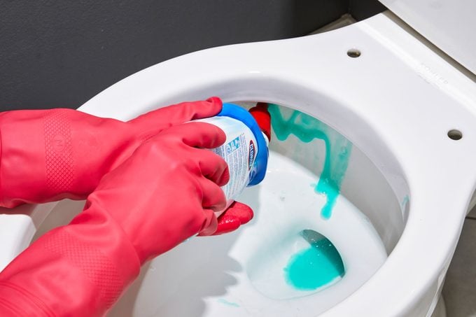 gloved hands squirting toilet bowl cleaner under the rim of the toilet bowl