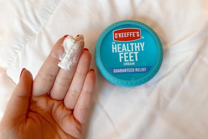 healthy feet Foot Cream on hand with the jar next to the hand resting on a bed