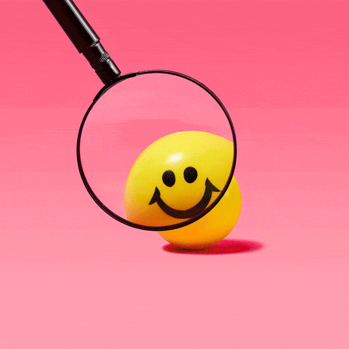 Magnifying glass magnifying different angles of a yellow smiley face ball to investigate what is happiness; pink background