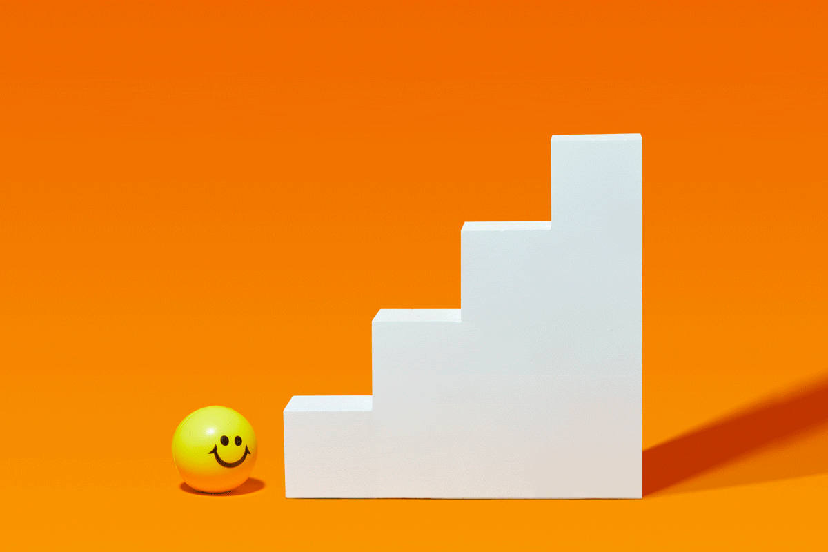 yellow ball with a smiley face bouncing his way up a white staircase; orange background