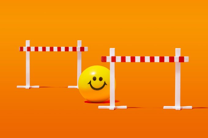 yellow smiley ball sitting between two track hurdles; orange background