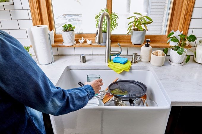 anonymous person clearing dishes out of the kitchen sink in preparation for cleaning