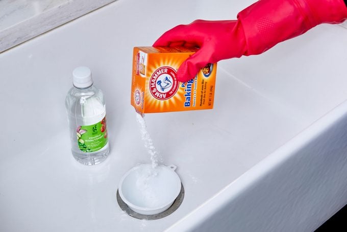 hand pouring baking soda into a funnel positioned in a kitchen sink drain