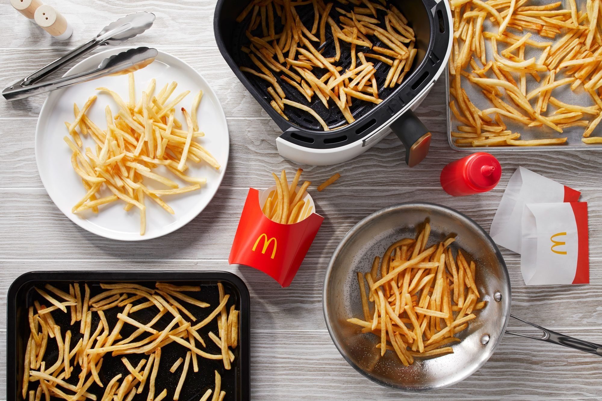 reheated mcdonalds fries on a plate, toaster oven pan, baking sheet, air fryer basket, and pan on light gray wood background