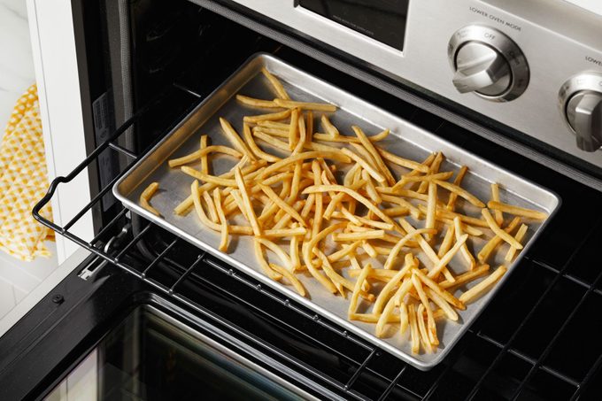 mcdonalds fries spread out on a baking sheet on a shelf in an open oven