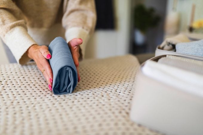 Hands Of Woman Rolling Clothes On Bed for packing a suitcase