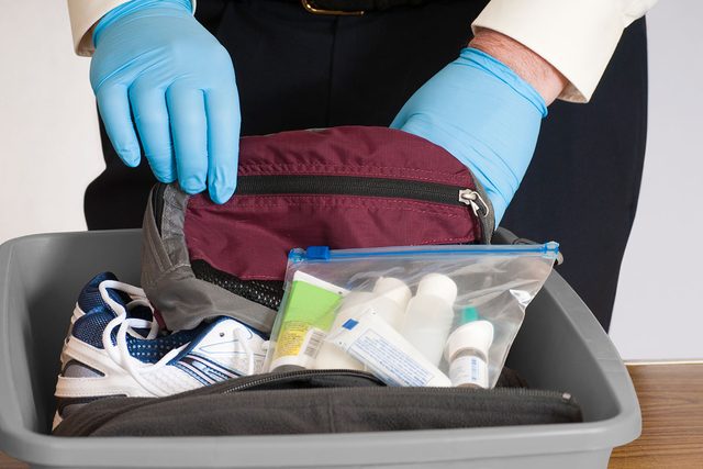 Gloved Hands of Airport Security Person Examines the content of a traveler's bin and belongings