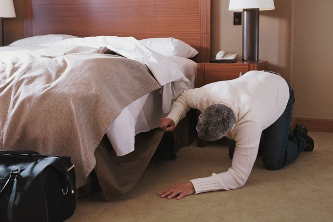 Man Kneeling On Floor In Hotel Room, Looking Under Bed
