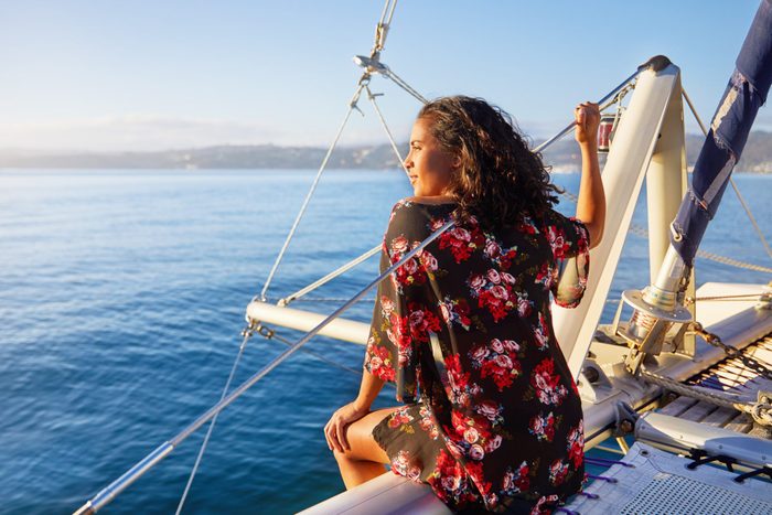 Serene young woman relaxing on sunny catamaran, looking out at blue ocean