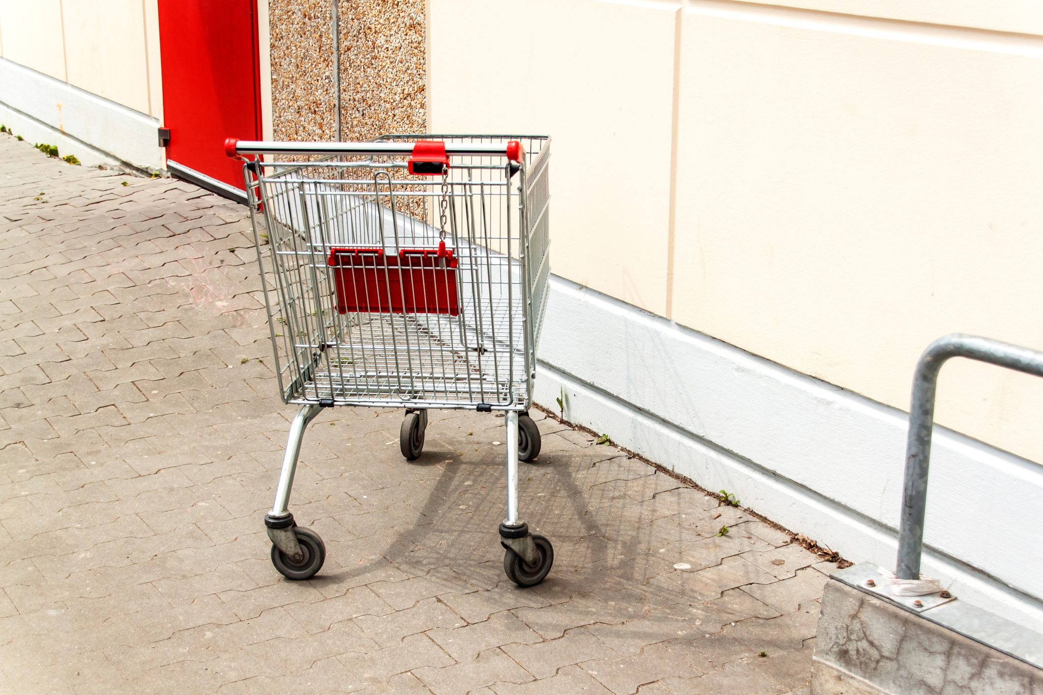 Empty shopping cart near the supermarket wall. Parking at the supermarket. Shopping symbol. Metal cart.