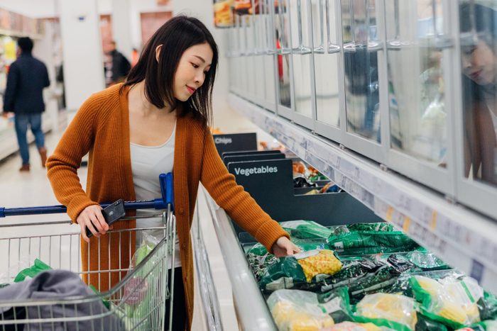 Young Asian woman shopping for frozen food with shopping cart in grocery store