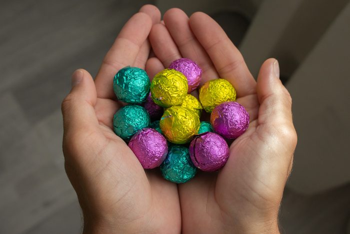 Colorful candies in hands, top view. Chocolate easter eggs in hands. Easter symbol. Sweet food concept. Hands holding group of shiny sweets.