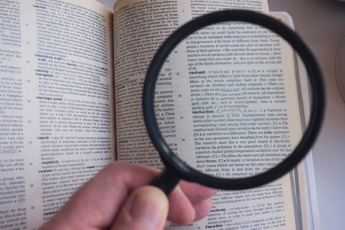 Hand of a man using a magnifying glass to look over dictionary pages 