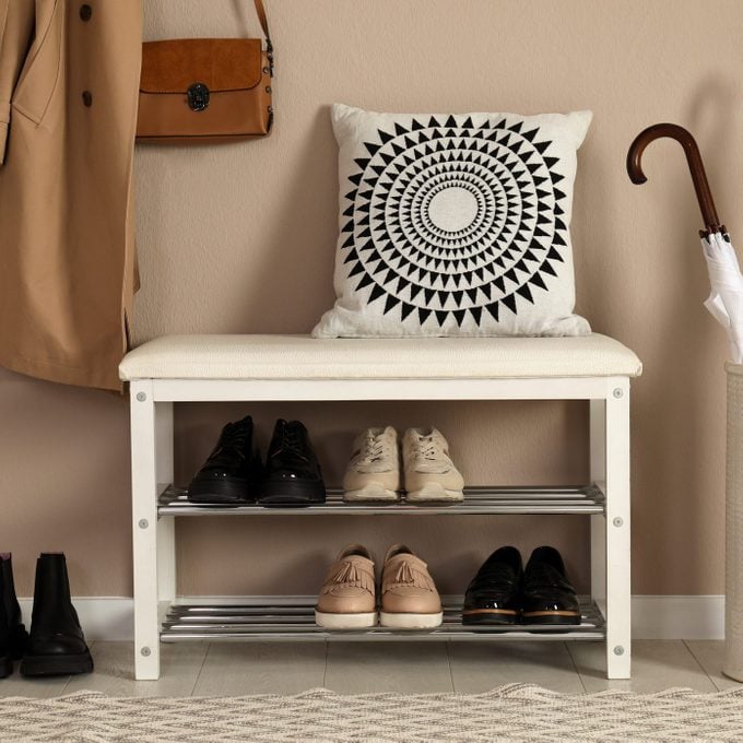 Stylish storage bench with different pairs of shoes near beige wall in hall