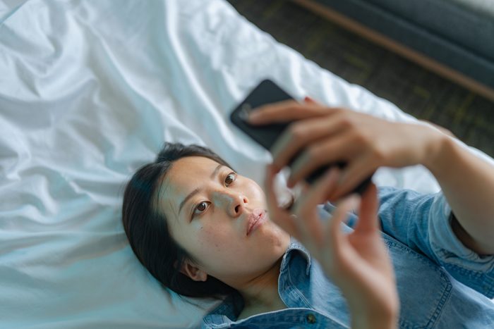 High angle view of young woman using smart phone while lying down on her bed