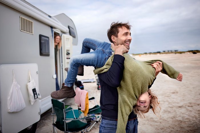 Playful father carrying girl at camper van on the beach