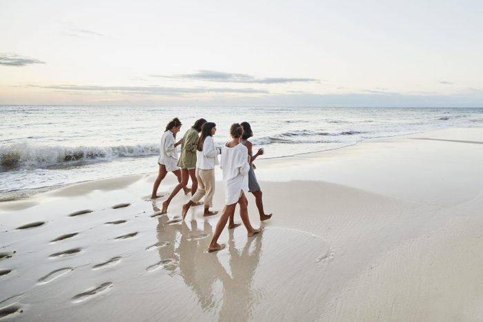 Wide shot of female friends walking on beach at tropical resort at sunrise