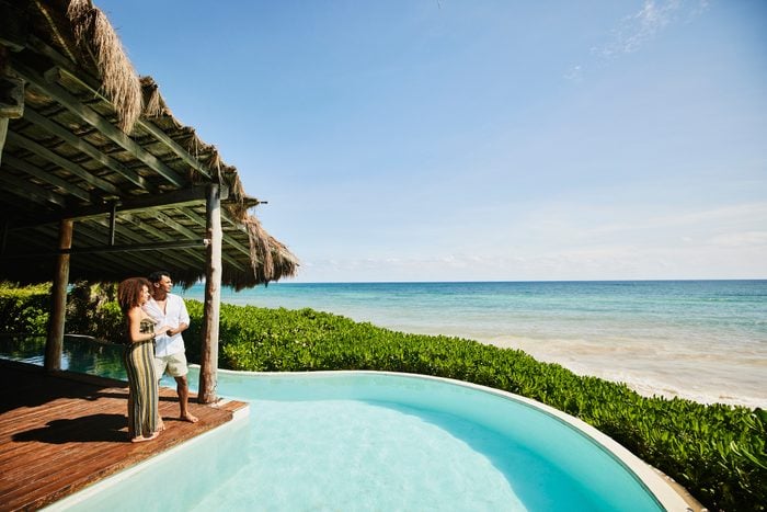 Wide shot of couple standing poolside at luxury tropical beachfront villa looking at view