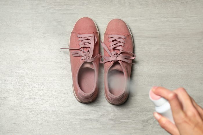 Woman spraying deodorant over pair of shoes at home, closeup