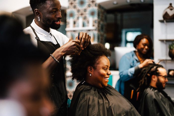 Male hairdresser cutting hair of smiling female customer at barber shop