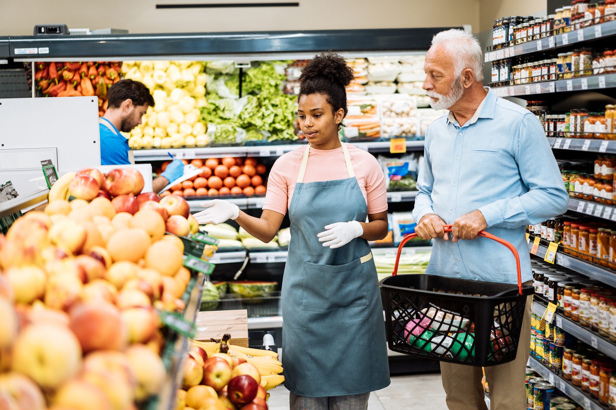 American employee in supermarket assisting senior customer while buying fruits and vegetables