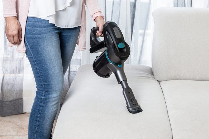 Crop woman cleaning sofa with vacuum cleaner