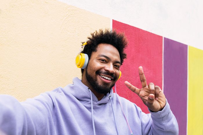 Happy man listening music through headphones taking selfie showing peace sign