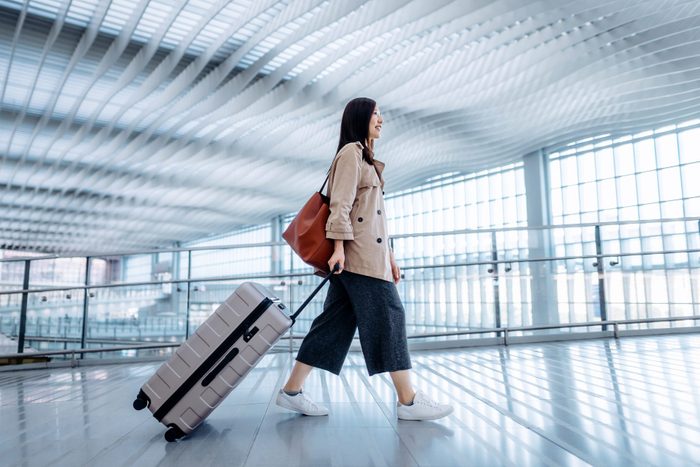 Side view of young Asian woman carrying suitcase walking in airport terminal. Ready to travel. Travel and vacation concept. Business person on business trip