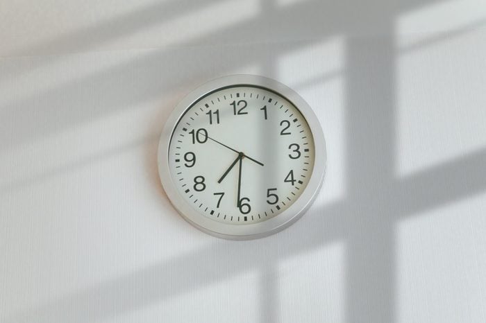 A simple white wall clock above a sunny window, in the afternoon