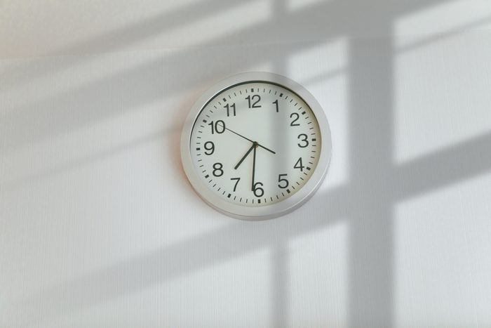 A simple white wall clock above a sunny window, in the afternoon