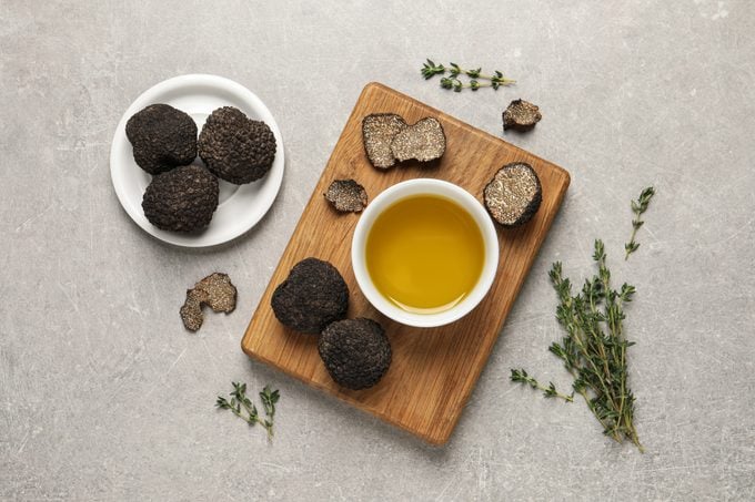 Fresh truffles, oil in bowl and thyme on light grey table, flat lay