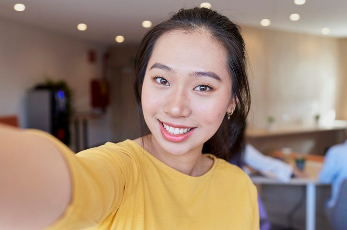 Portrait of young asian woman holding camera and smiling with unfocused background