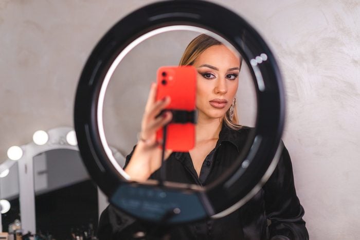 Beautiful young make-up artist taking selfies while posing in front of a ring light