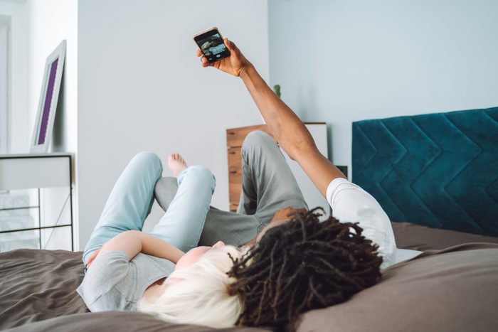 Selfie playing and fooling around. Multiracial and multicultural black and white skin couple lying on a bed and using smartphone for selfie