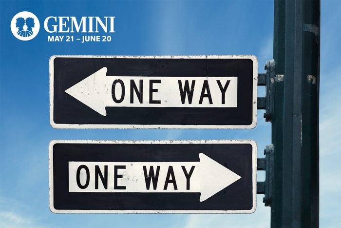 Two one-way signs on a pole pointing in different directions against a blue sky