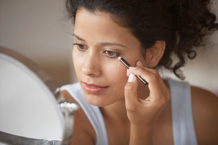 Woman applying eyeliner looking at mirror