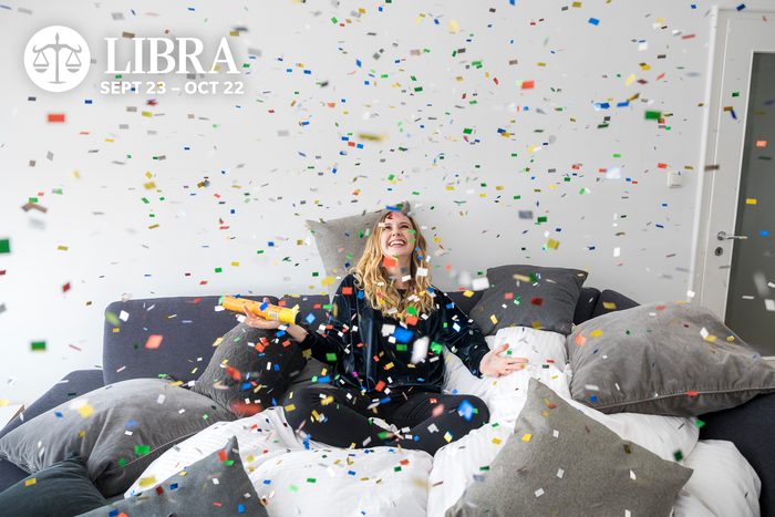 Laughing young woman having fun with flying confetti at home