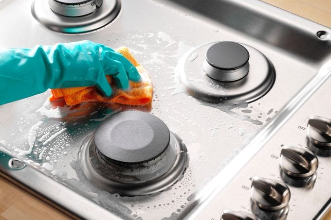 hand scrubbing the surface of a gas stove top