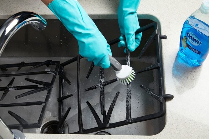 hands scrubbing the gas stove grates in a kitchen sink