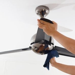 Asian man wearing a protective mask cleaning ceiling fan at home