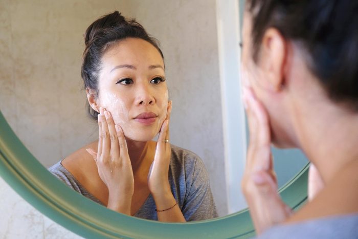 woman applying a facial cleanser in the mirror