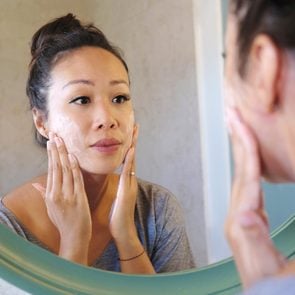 woman applying a facial cleanser in the mirror