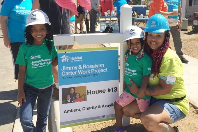 Ambera Pruitt and daughters standing in front of a house sign