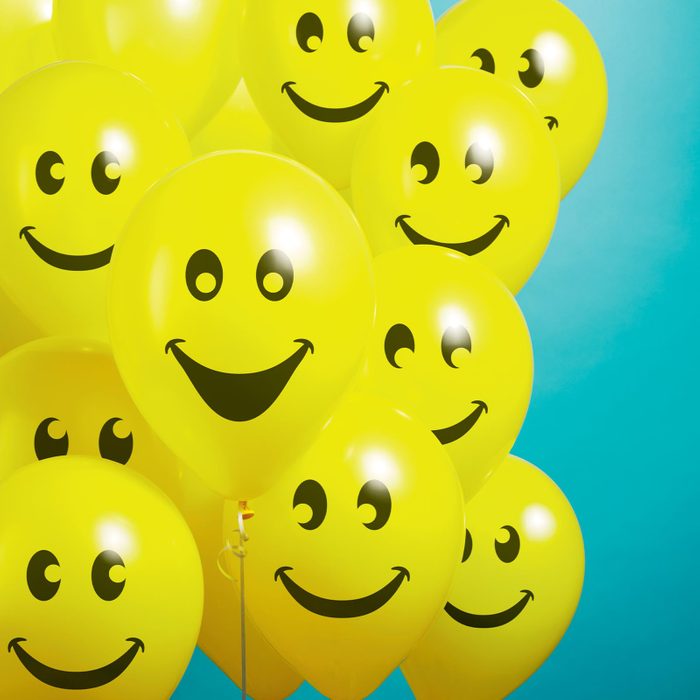 A cluster of floating yellow smiley face balloons on a teal background