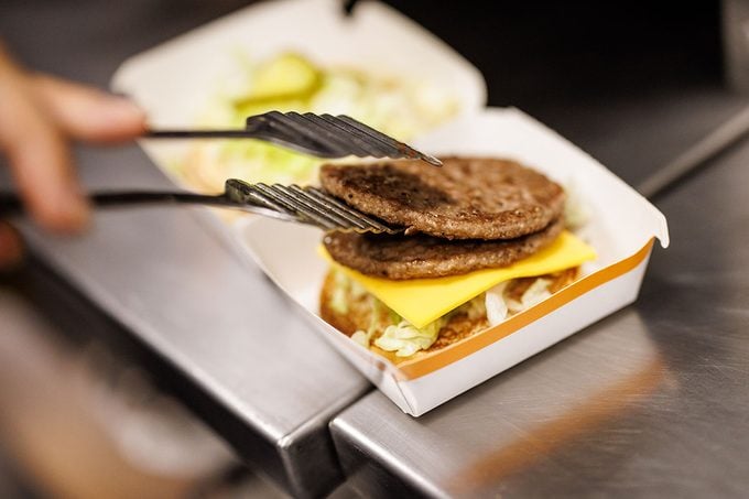 An Employee Places a patty on a hamburger bun to prepare a Big Mac Sandwich