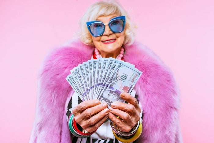 Cool And Stylish Senior Old Woman With Fashionable Clothes and holding money on a pink background
