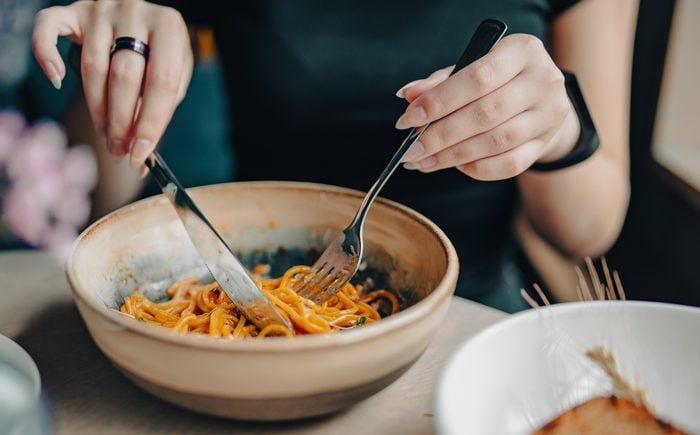 Italian food. woman hand holding fork and knife with spaghetti bolognese in bowl